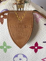 Close-up of a Louis Vuitton monogram bag showing a tan leather shield-shaped tag with 'LOUIS VUITTON PARIS made in France' embossed on it, attached to a gold-tone zipper pull on a white patterned canvas background.
