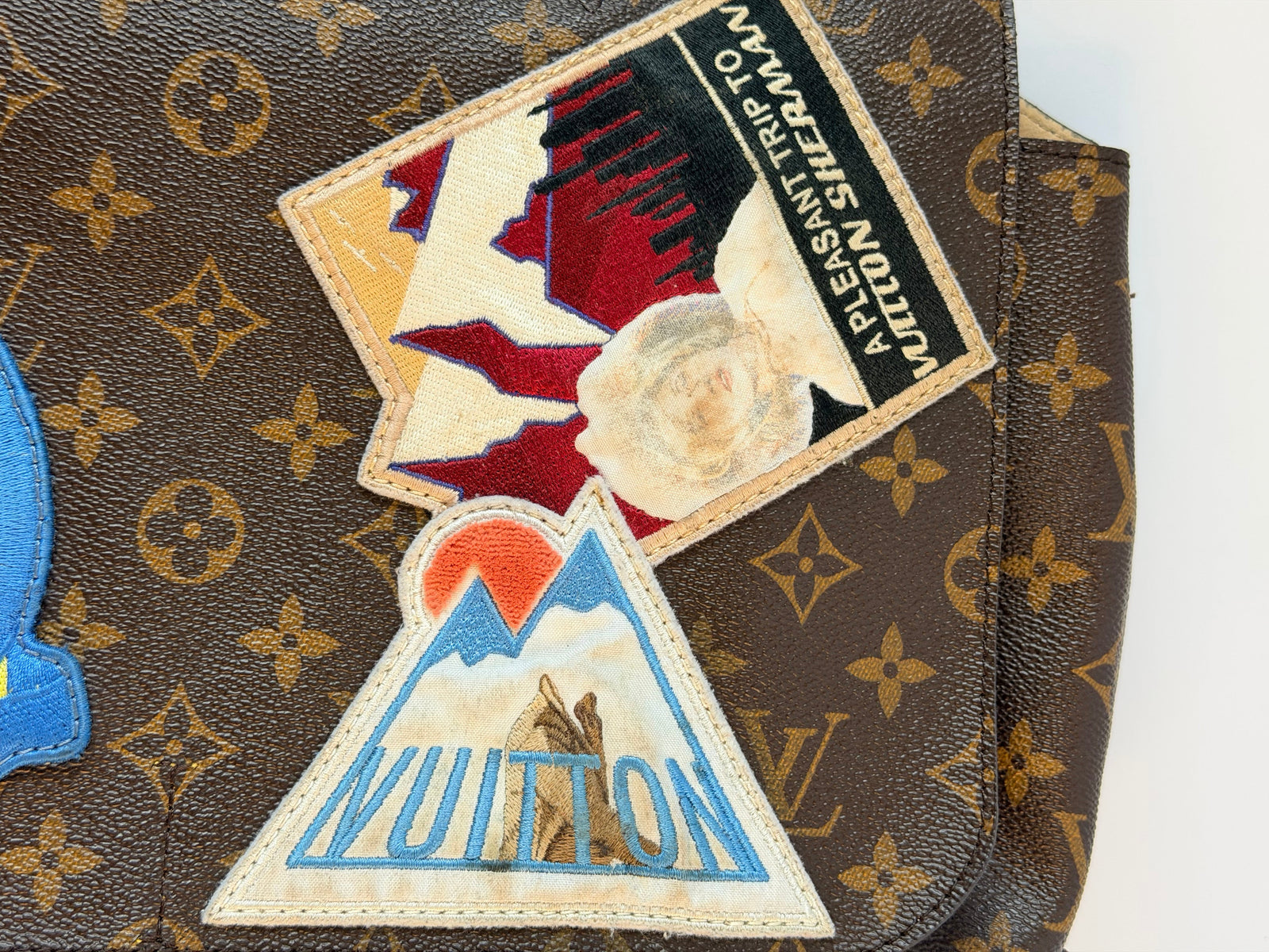 Close-up of a brown Louis Vuitton monogram bag with two decorative embroidered patches attached on the front.