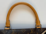 Close-up of a tan leather handle attached to a dark brown monogram canvas bag, showing metal hardware and yellow stitching on a light gray background.