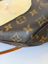 Close-up of a Louis Vuitton monogram canvas bag corner showing the brown coated canvas with tan/gold LV monogram pattern and a light beige suede or leather tab.
