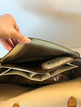 A close-up of a hand opening a beige leather clutch or wallet, showing the interior card slots and a card with a blue and gold logo.